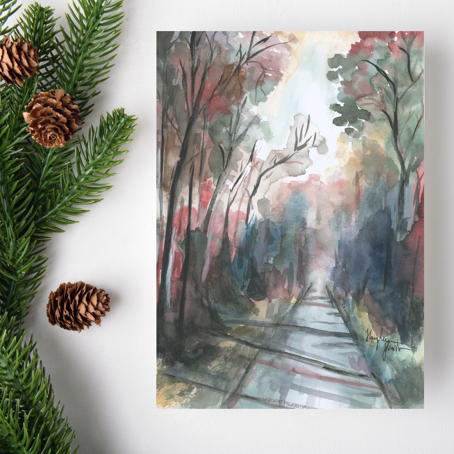 Flat cardstock note card featuring original watercolor piece Forest Road on a white background. Green pine fronds with brown pinecones decorate the left side.