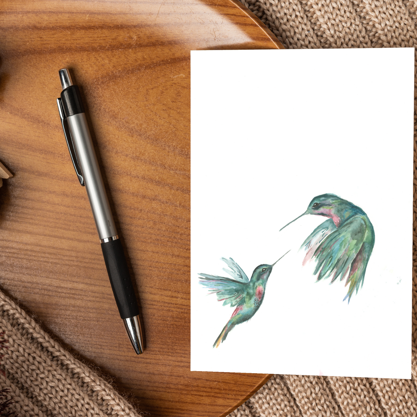 A card with hummingbird illustration next to a pen on a wooden surface