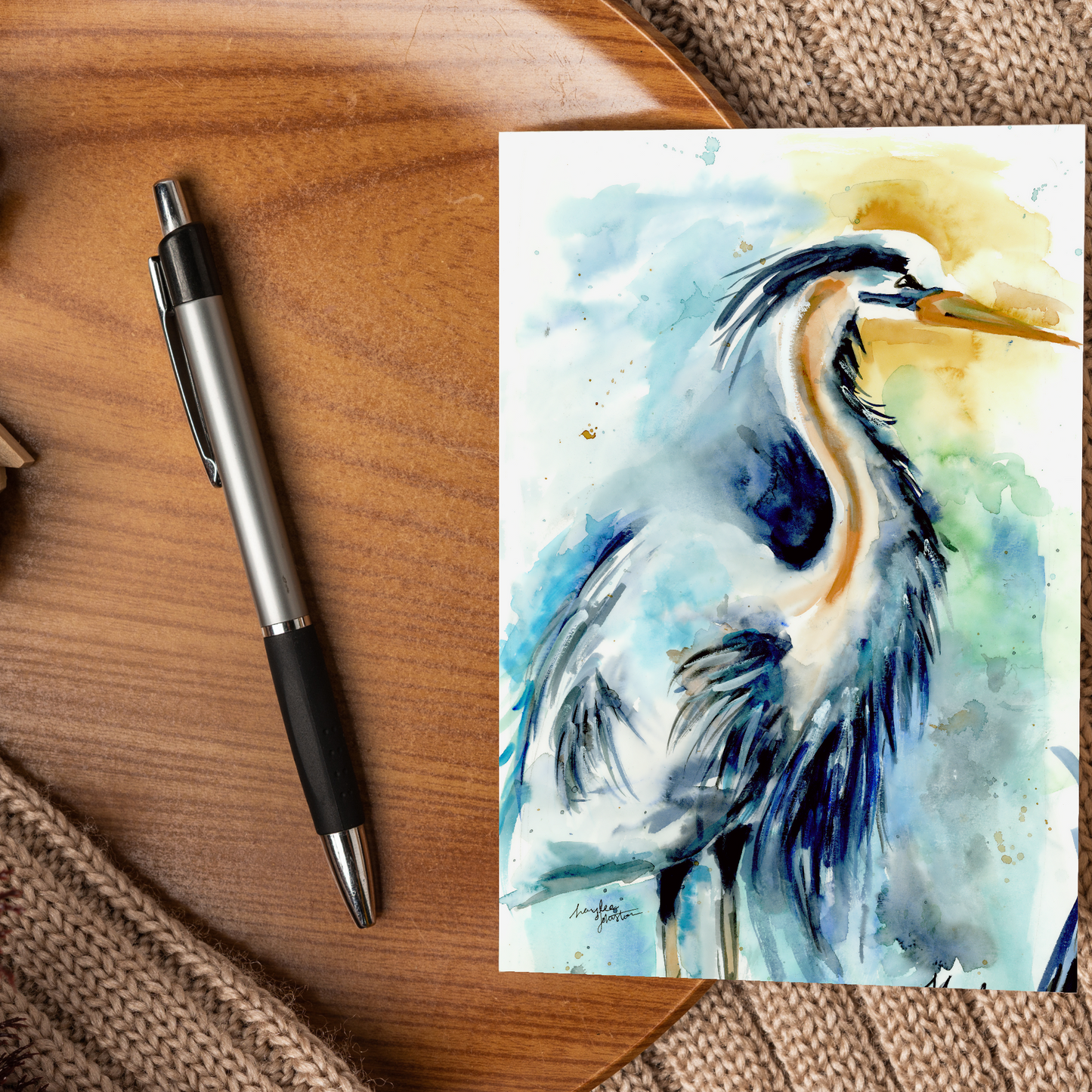Flat cardstock note card featuring original watercolor piece Male Heron displayed on a wooden surface beside a black and silver pen.