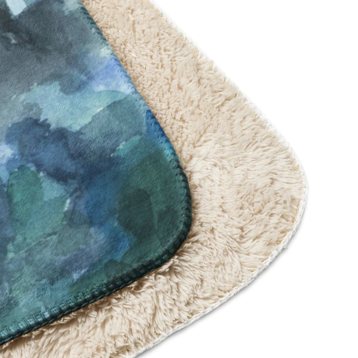 Close-up of tan sherpa blanket with soft cream fleece and blue-green watercolor design on edge
