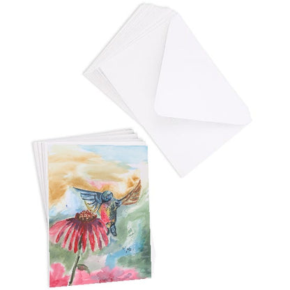 A stack of flat cardstock note cards featuring original watercolor piece A Jeweled Messenger next to a stack of the matching euro flap envelopes.