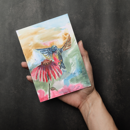 Flat cardstock note card featuring original watercolor piece A Jeweled Messenger in a person's right hand. The background transitions from black at the bottom to a dull gray at the top.