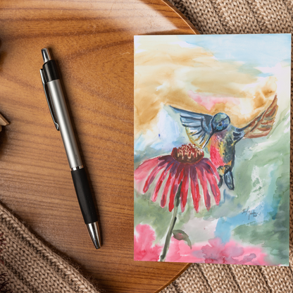 Flat cardstock note card featuring original watercolor piece A Jeweled Messenger displayed on a wooden surface beside a black and silver pen.