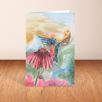 Folding cardstock greeting card featuring original watercolor piece A Jeweled Messenger standing upright on a wooden table.