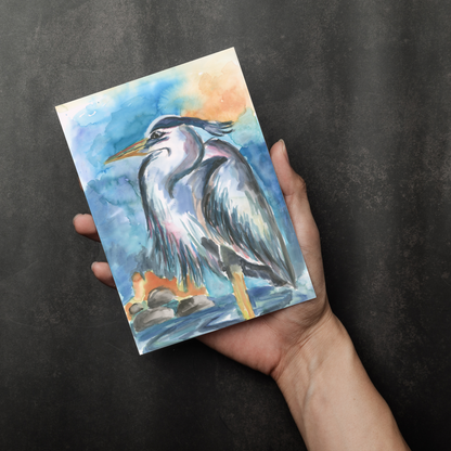 Flat cardstock note card featuring original watercolor piece Dark Heron in a person's right hand. The background transitions from black at the bottom to a dull gray at the top.