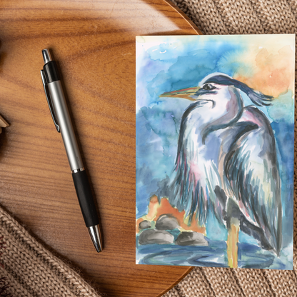 Flat cardstock note card featuring original watercolor piece Dark Heron displayed on a wooden surface beside a black and silver pen.