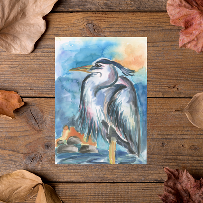 Flat cardstock note card featuring original watercolor piece Dark Heron styled on rustic wooden boards with dried autumn leaves.