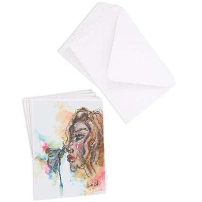 A stack of flat cardstock note cards featuring original watercolor piece Dragonfly Girl next to a stack of the matching euro flap envelopes.