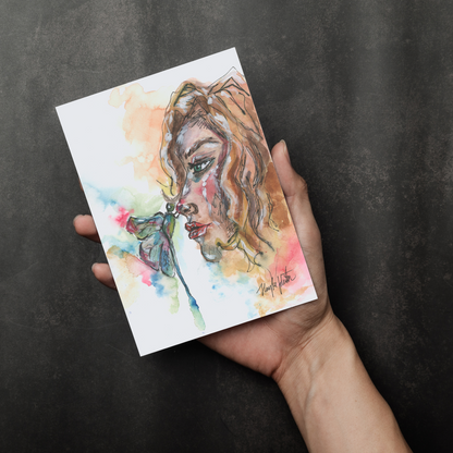 Flat cardstock note card featuring original watercolor piece Dragonfly Girl in a person's right hand. The background transitions from black at the bottom to a dull gray at the top.