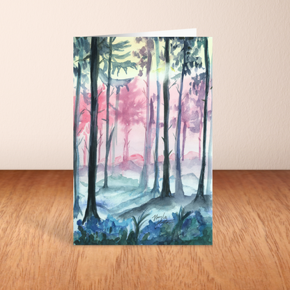 Folding cardstock greeting card featuring original watercolor piece Fairy Forest standing upright on a wooden table.