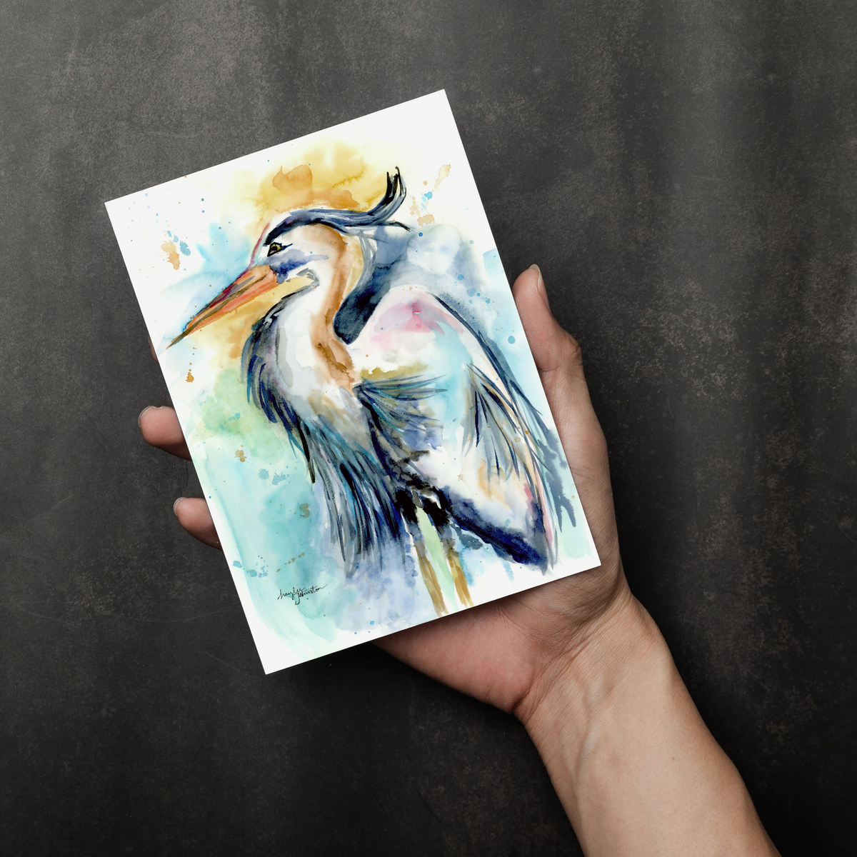 Flat cardstock note card featuring original watercolor piece Female Heron in a person's right hand. The background transitions from black at the bottom to a dull gray at the top.