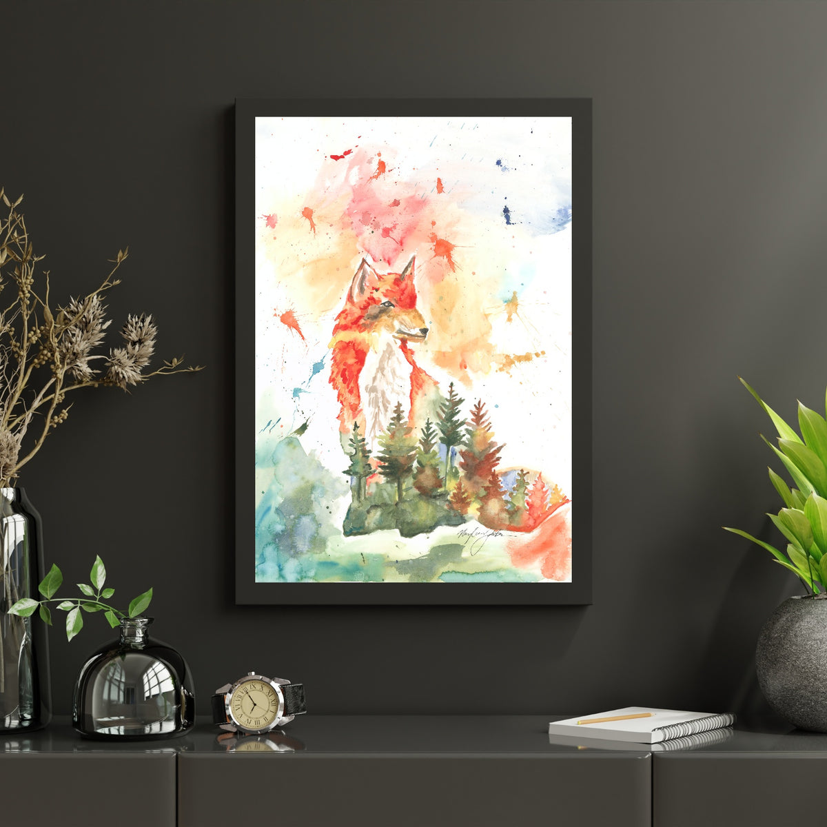Giclée Forest Fox in a black frame hangs on a charcoal wall above a matching dark gray sideboard. The sideboard is styled with smoked glass vessels, dried botanicals, a wristwatch, and a spiral notebook with a pencil, with a leafy plant in a dark round vase to the right.