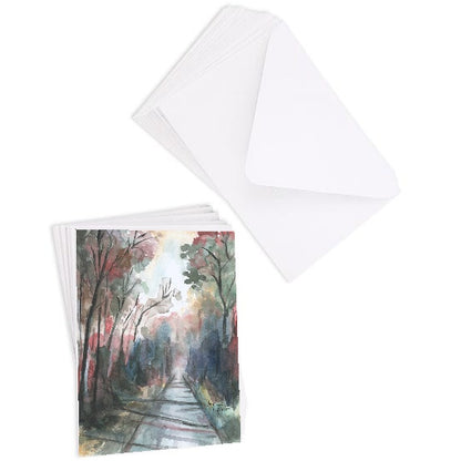A stack of flat cardstock note cards featuring original watercolor piece Forest Road next to a stack of the matching euro flap envelopes.