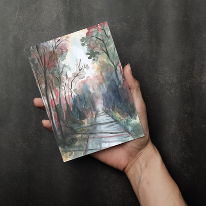 Flat cardstock note card featuring original watercolor piece Forest Road in a person's right hand. The background transitions from black at the bottom to a dull gray at the top.
