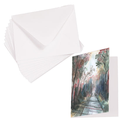 Folding cardstock greeting card featuring original watercolor piece Forest Road laying next to a stack of euro flap envelopes.