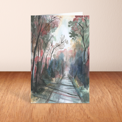 Folding cardstock greeting card featuring original watercolor piece Forest Road standing upright on a wooden table.