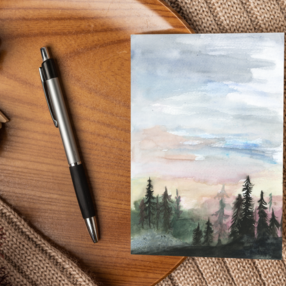 Flat cardstock note card featuring original watercolor piece Forest Skyline displayed on a wooden surface beside a black and silver pen.