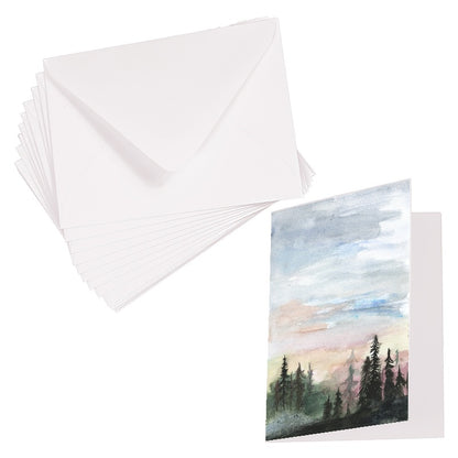 Folding cardstock greeting card featuring original watercolor piece Forest Skyline laying next to a stack of euro flap envelopes.