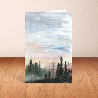Folding cardstock greeting card featuring original watercolor piece Forest Skyline standing upright on a wooden table.