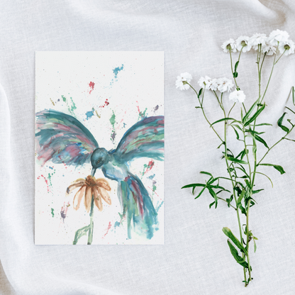 Flat cardstock note card featuring original watercolor piece Hovering Hummingbird on a white linen background next to fresh white flowers.