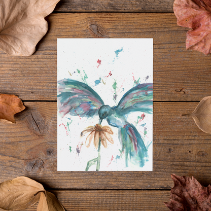 Flat cardstock note card featuring original watercolor piece Hovering Hummingbird styled on rustic wooden boards with dried autumn leaves.