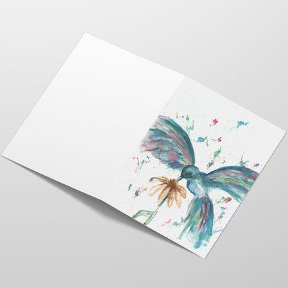 Folding cardstock greeting card featuring original watercolor piece Hovering Hummingbird laying open in a table with the outside facing up.