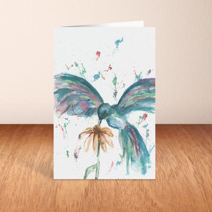 Folding cardstock greeting card featuring original watercolor piece Hovering Hummingbird standing upright on a wooden table.