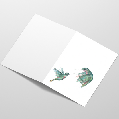 Folding cardstock greeting card featuring original watercolor piece Hummingbird Duel laying open in a table with the outside facing up.