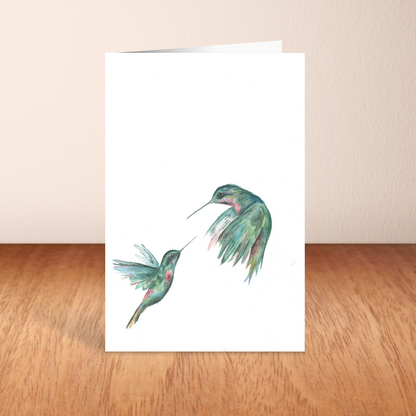 Folding cardstock greeting card featuring original watercolor piece Hummingbird Duel standing upright on a wooden table.