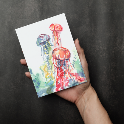 Flat cardstock note card featuring original watercolor piece Jellyfish Bloom in a person's right hand. The background transitions from black at the bottom to a dull gray at the top.