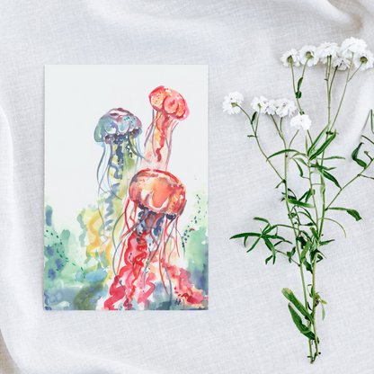 Flat cardstock note card featuring original watercolor piece Jellyfish Bloom on a white linen background next to fresh white flowers.