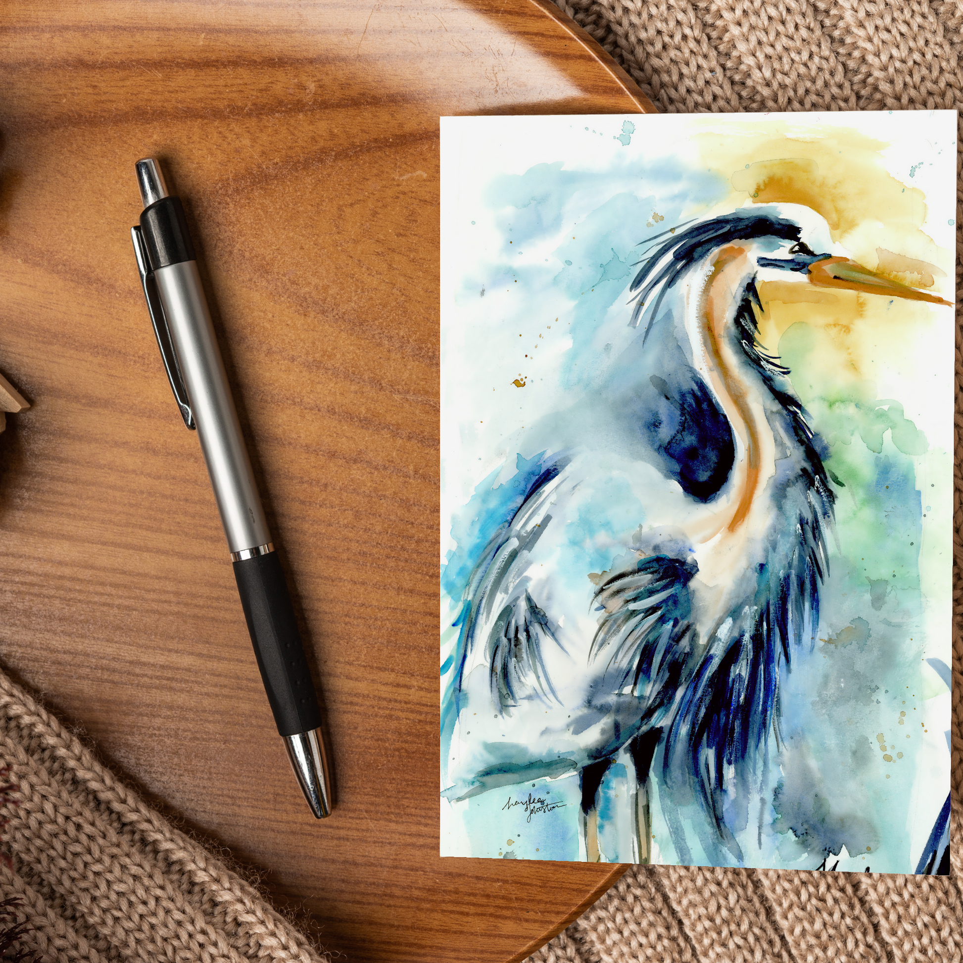 Flat cardstock note card featuring original watercolor piece Male Heron displayed on a wooden surface beside a black and silver pen.