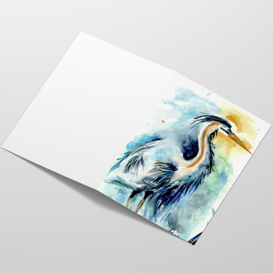 Folding cardstock greeting card featuring original watercolor piece Male Heron laying open in a table with the outside facing up.