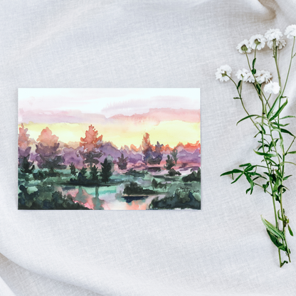 Flat cardstock note card featuring original watercolor piece Misty Sunrise on a white linen background next to fresh white flowers.