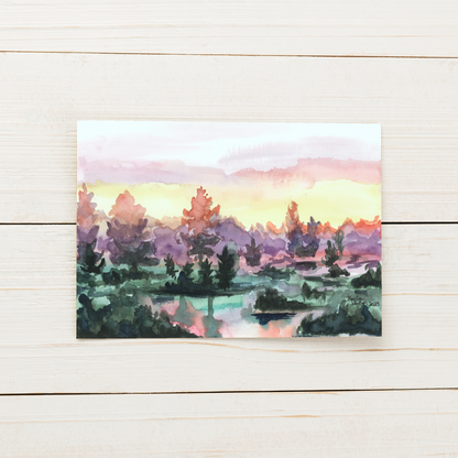 Flat cardstock note card featuring original watercolor piece Misty Sunrise displayed on a white painted wooden surface.