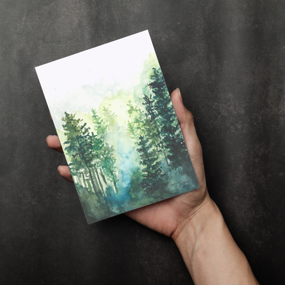 Flat cardstock note card featuring original watercolor piece Morning Forest in a person's right hand. The background transitions from black at the bottom to a dull gray at the top.