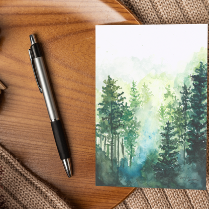 Flat cardstock note card featuring original watercolor piece Morning Forest displayed on a wooden surface beside a black and silver pen.