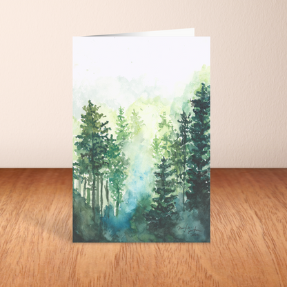 Folding cardstock greeting card featuring original watercolor piece Morning Forest standing upright on a wooden table.