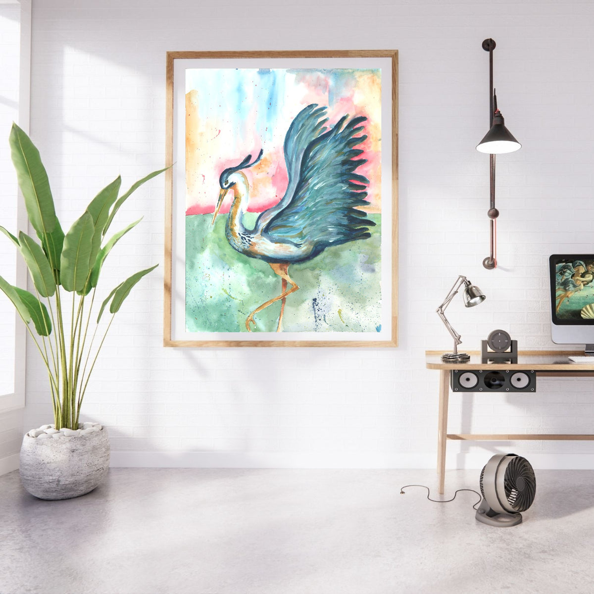 Giclée Morning Glories in a large oak frame with white matting hangs on a white brick wall in a bright studio. A tall leafy plant in a stone planter stands to the left, and a light wood desk with a computer monitor, adjustable lamp, and speaker sits to the right beneath an industrial wall light.