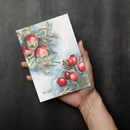 Flat cardstock note card featuring original watercolor piece Red Apples and Rosehips in a person's right hand. The background transitions from black at the bottom to a dull gray at the top.