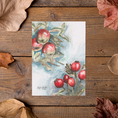 Flat cardstock note card featuring original watercolor piece Red Apples and Rosehips styled on rustic wooden boards with dried autumn leaves.