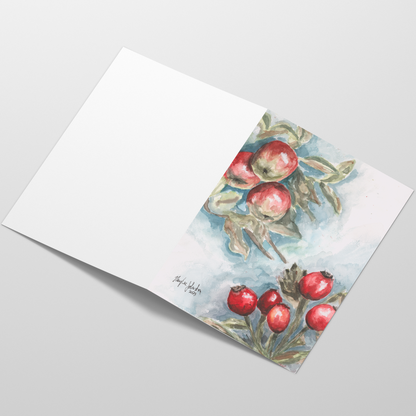 Folding cardstock greeting card featuring original watercolor piece Red Apples and Rosehips laying open in a table with the outside facing up.