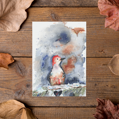 Flat cardstock note card featuring original watercolor piece Red Bellied Woodpecker styled on rustic wooden boards with dried autumn leaves.