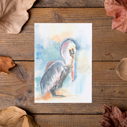 Flat cardstock note card featuring original watercolor piece Shy Pelican styled on rustic wooden boards with dried autumn leaves.