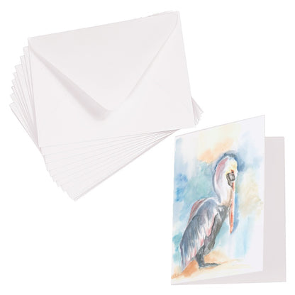 Folding cardstock greeting card featuring original watercolor piece Shy Pelican laying next to a stack of euro flap envelopes.