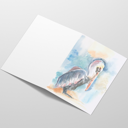 Folding cardstock greeting card featuring original watercolor piece Shy Pelican laying open in a table with the outside facing up.